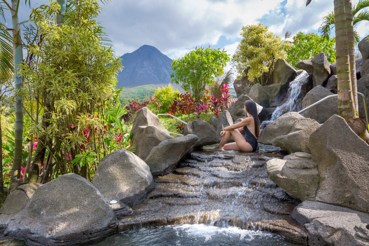 Dame im Vordergrund in Thermalbädern die Sicht auf den Vulkan Arenal gerichtet